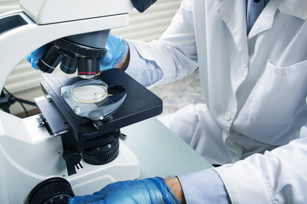 Photo of a professional microscope close-up with chemist scientific researcher hands using microscope in the laboratory interior.